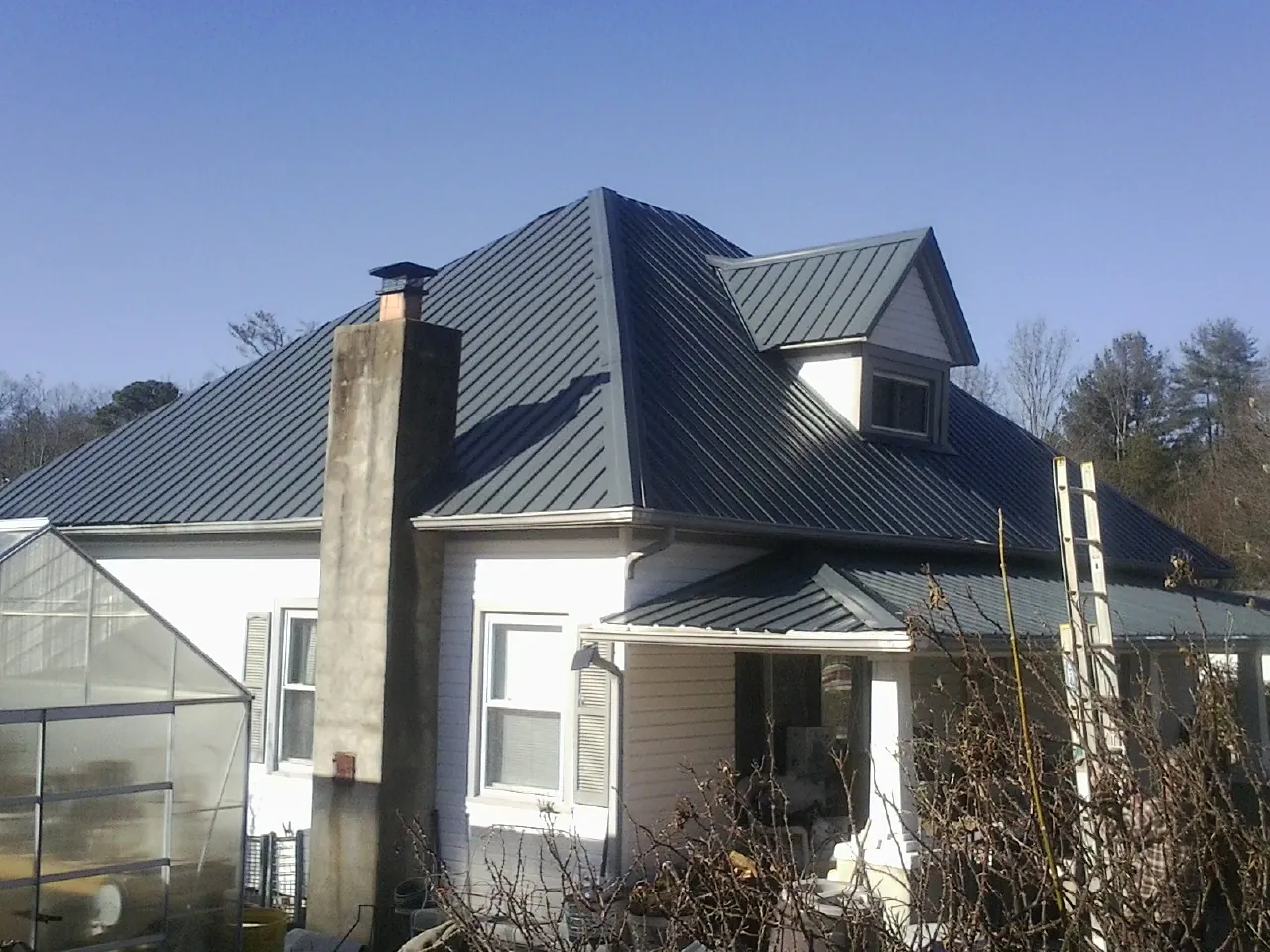 Dark blue standing seam metal roof on a white farmhouse with dormer — Slate & Tile Roof Repair by Roofing Brothers in Only