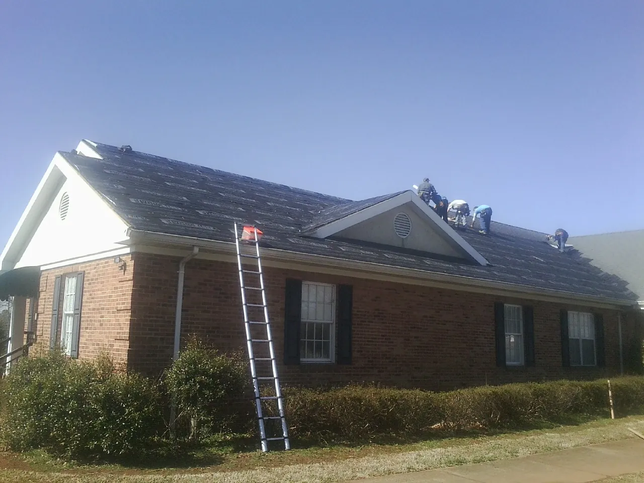 Crew tearing shingles off a brick ranch roof with a ladder set — Emergency Roof Repair work by our crew in Only
