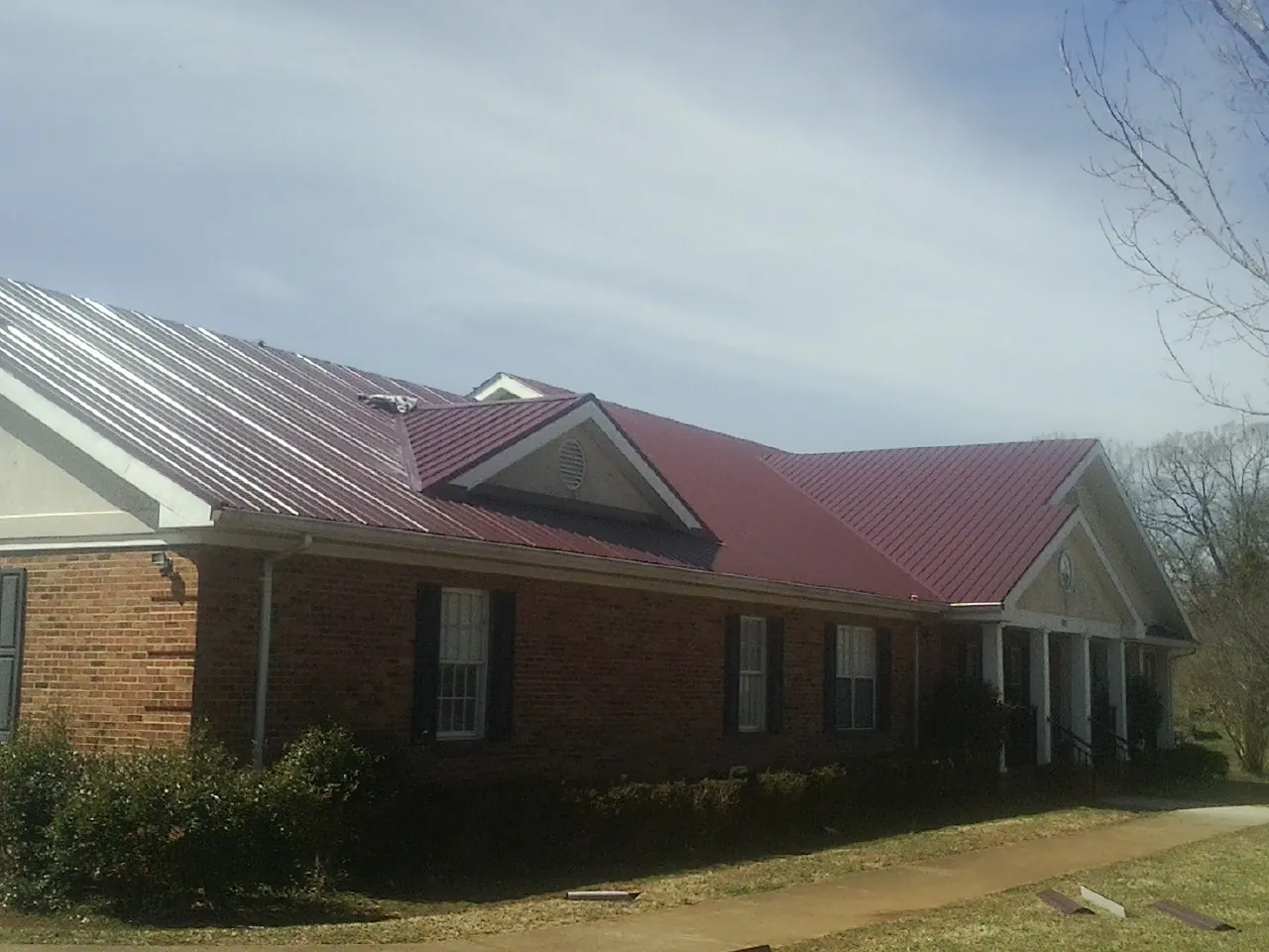 Red metal roof with gabled entries on a long brick building, from a Hail Damage Roof Repair job in Only