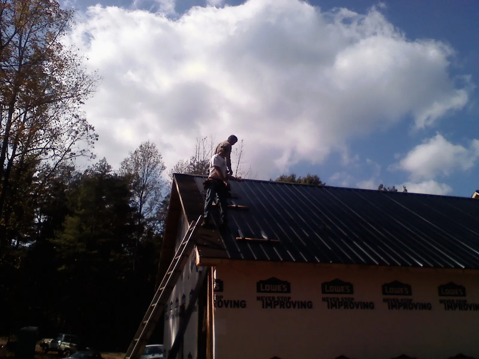 Roofer fastening dark metal panels high against a cloudy sky, from a Roof Inspection job in Only