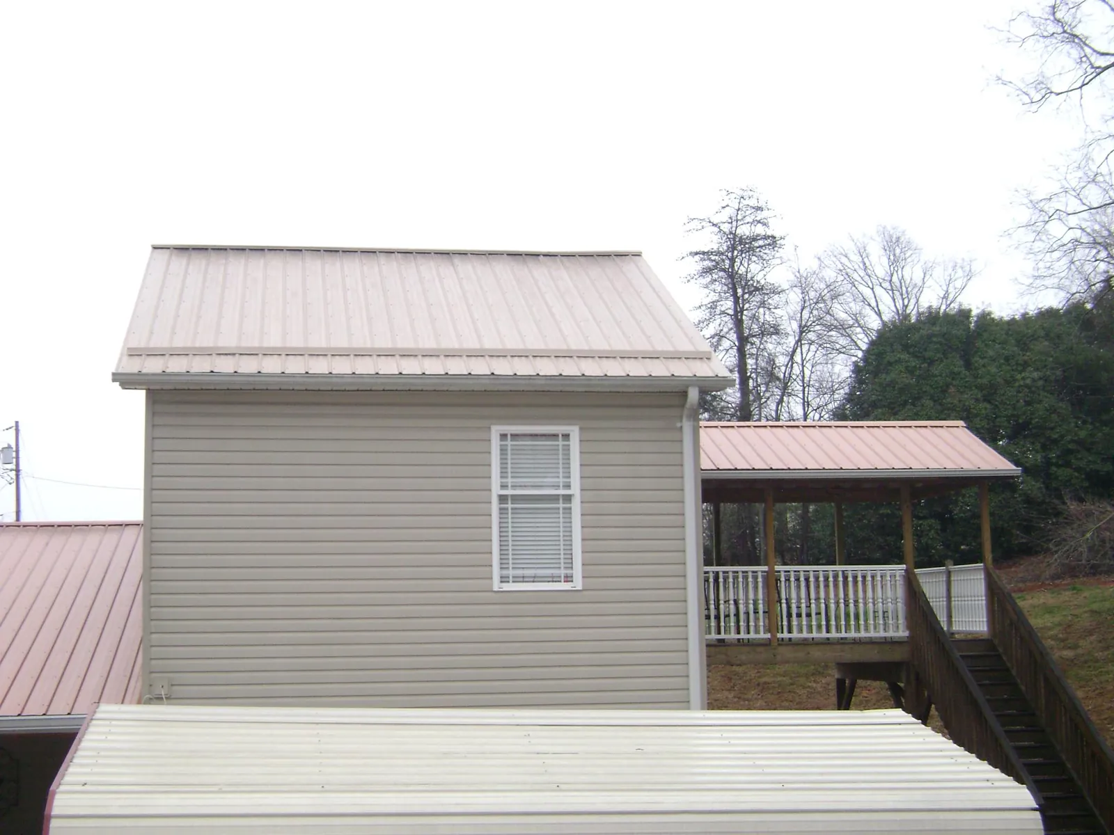 Tan metal roofs on a two story addition and attached porch, from a Roof Replacement job in Only